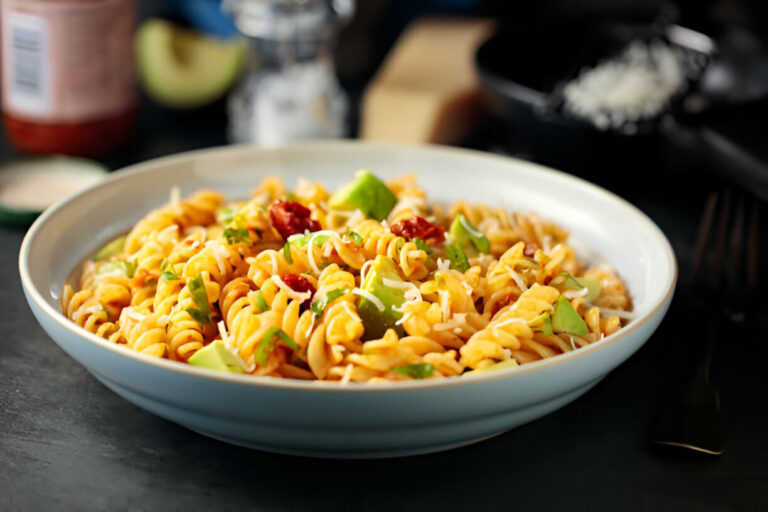 A bowl of colorful pasta topped with green herbs and sun-dried tomatoes.