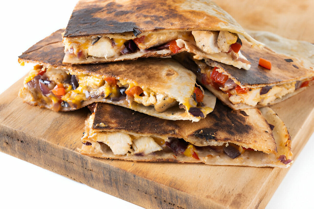 A stack of grilled quesadillas with chicken and colorful vegetables placed on a wooden cutting board.