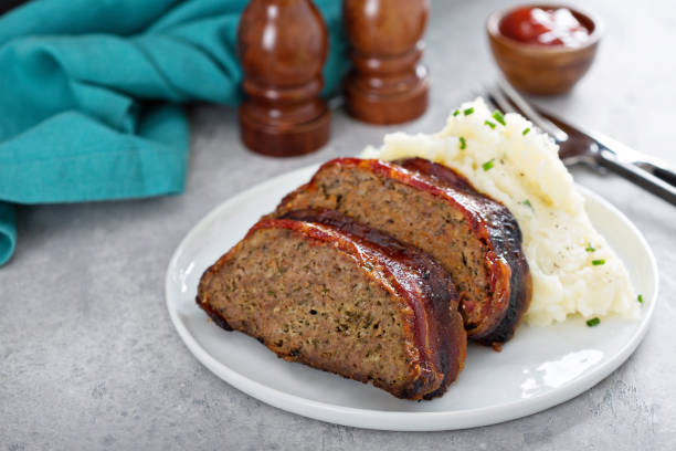 Sliced meatloaf served on a plate with mashed potatoes and condiments.