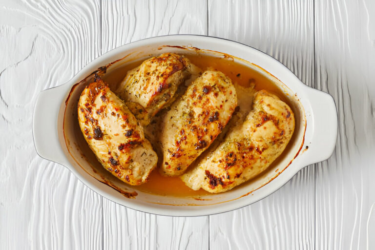 Cooked chicken breasts in a white casserole dish on a wooden surface.