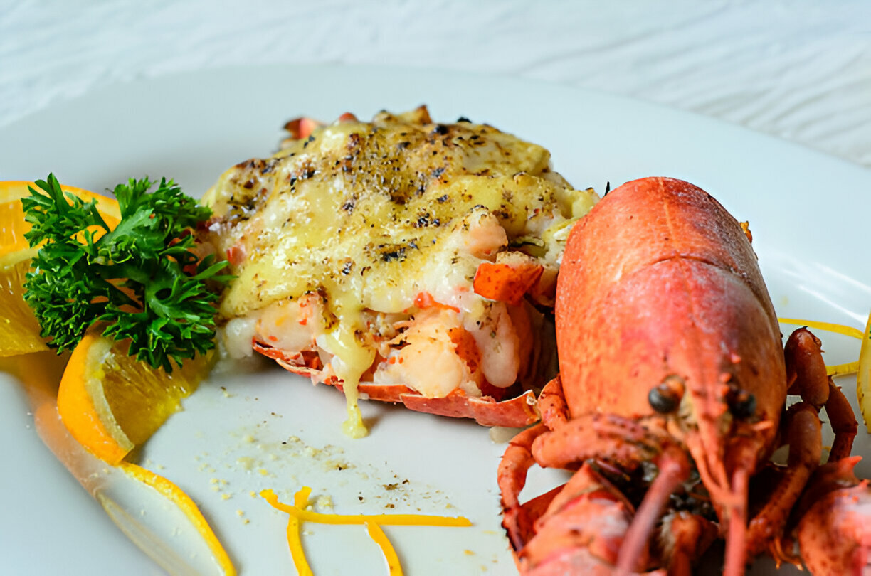 A gourmet lobster dish served with cheese on a white plate, garnished with parsley and orange slices.