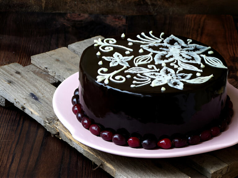 A beautifully decorated chocolate cake with floral designs on top, garnished with red berries on a pink plate.