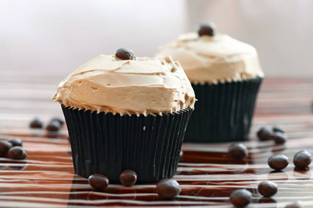 Two chocolate cupcakes with creamy frosting and coffee beans on top, placed on a wooden table.