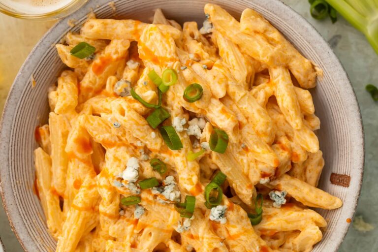 Creamy penne pasta topped with chopped green onions and blue cheese in a ceramic bowl