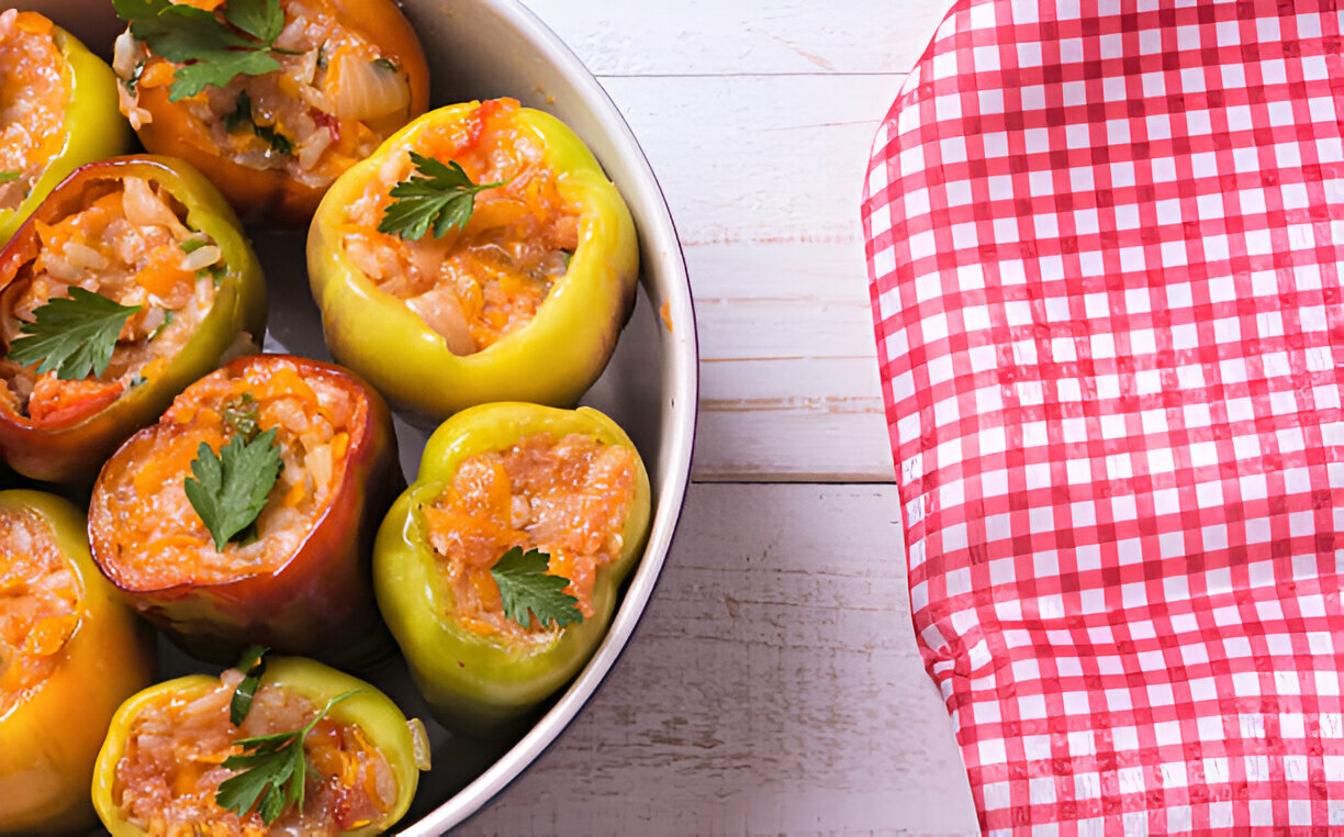 A tray filled with colorful stuffed peppers, garnished with parsley, alongside a red and white checkered cloth.