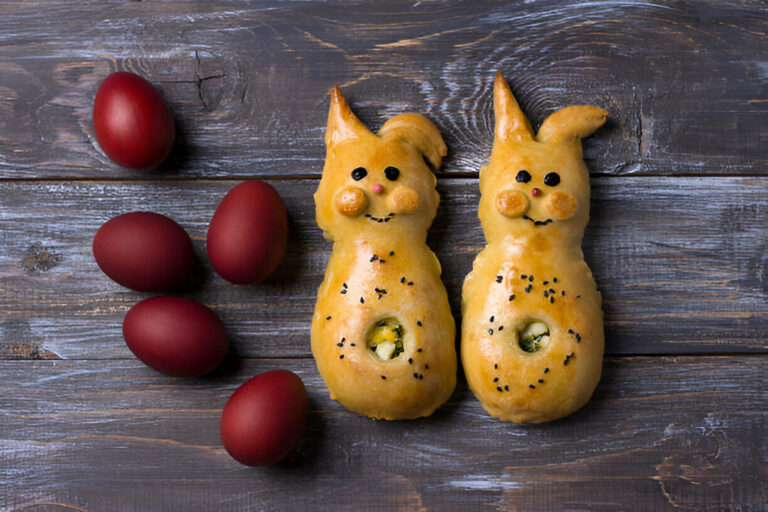 Two cute bunny-shaped pastries with red eggs on a wooden table