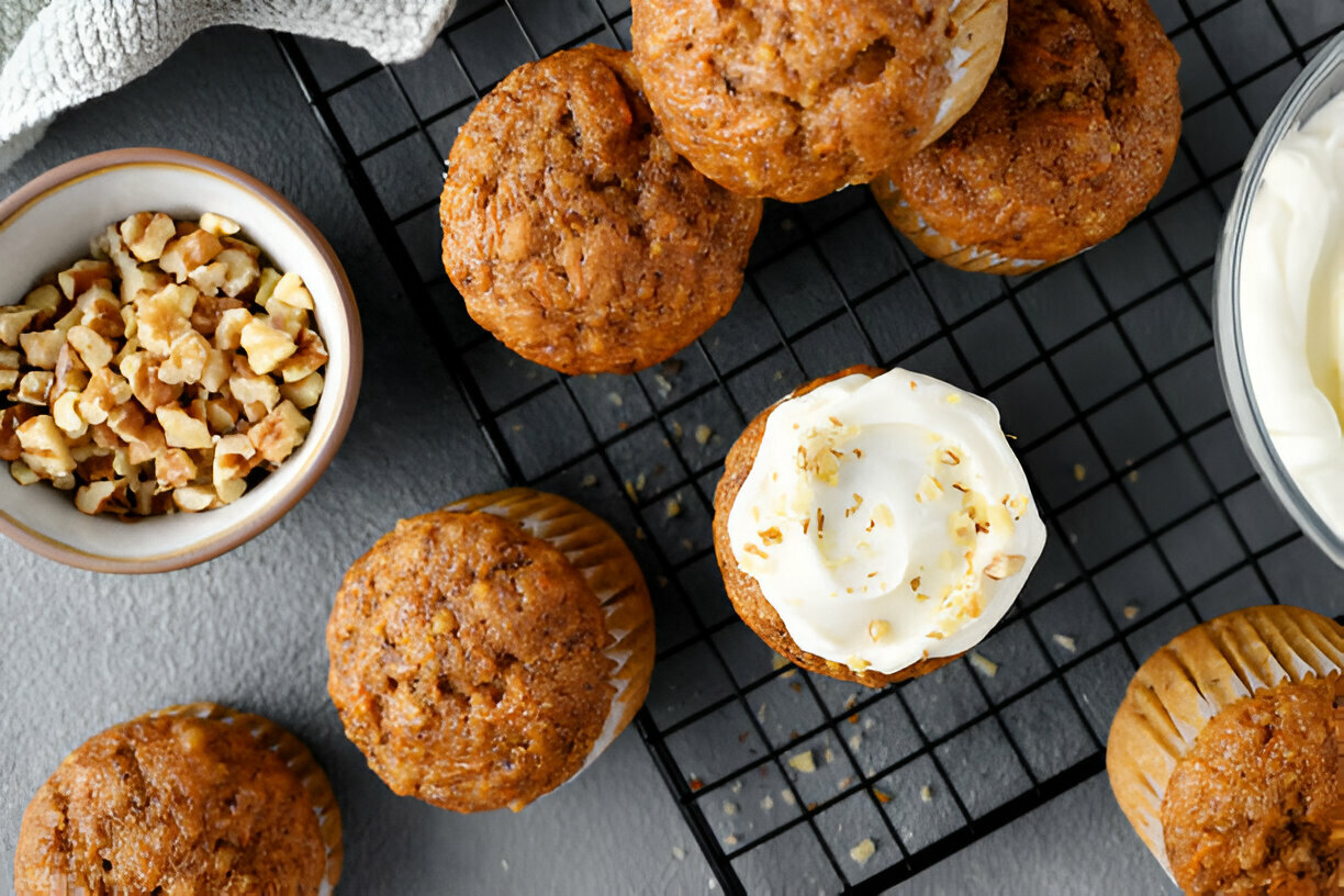 A delicious display of freshly baked cupcakes topped with cream cheese frosting and chopped walnuts on a cooling rack, with additional chopped walnuts in a small bowl.