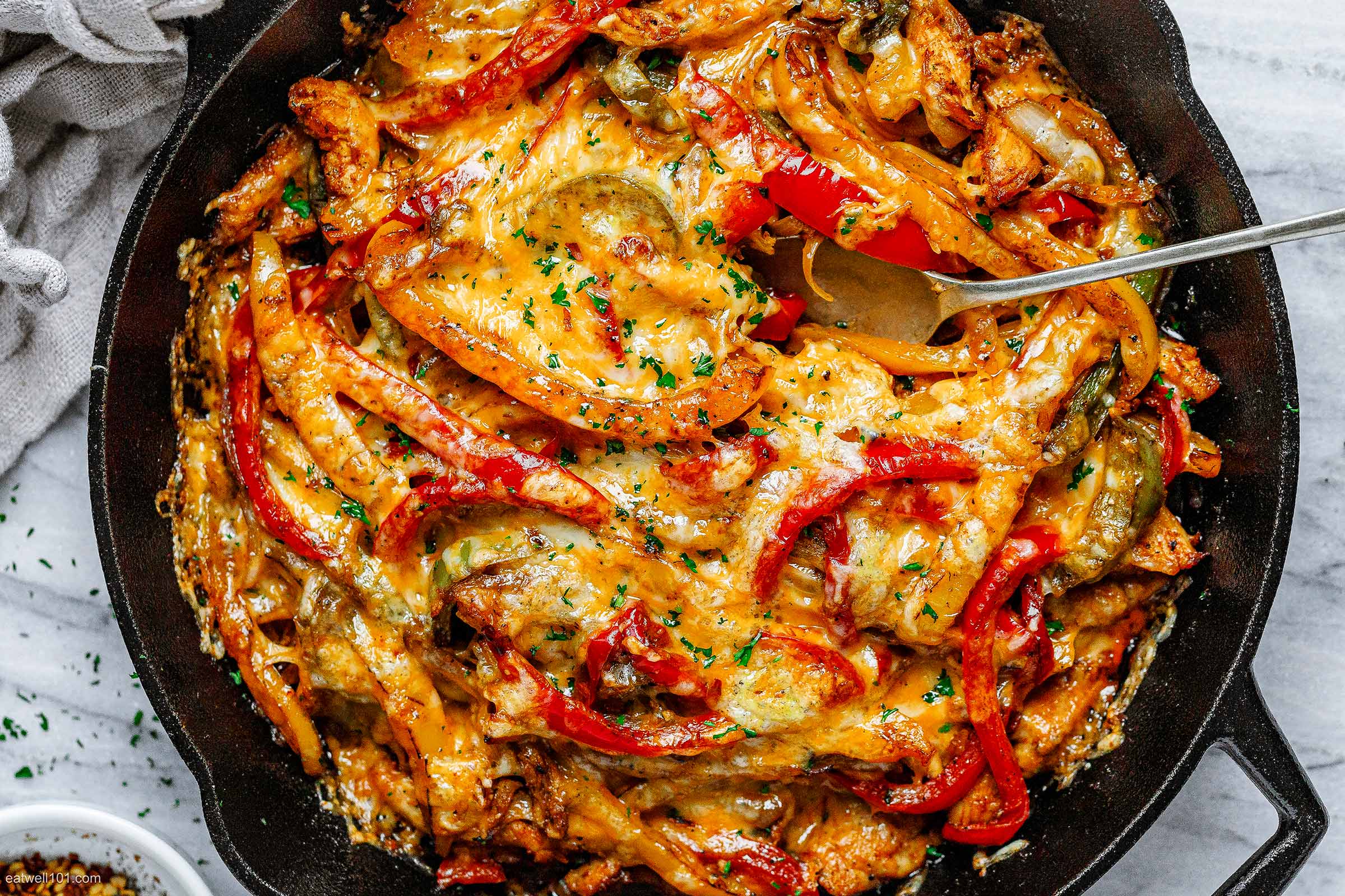 A delicious skillet dish topped with melted cheese, colorful bell peppers, and herbs.