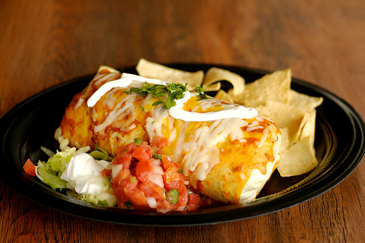 A delicious plate of burrito served with salsa, sour cream, lettuce, and tortilla chips.