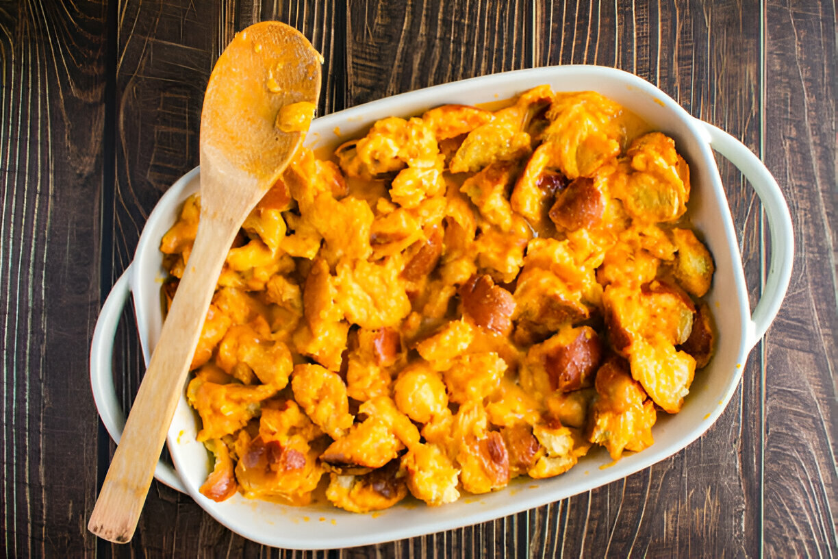 A creamy casserole dish filled with bread pieces and melted cheese, with a wooden spoon resting on the side.