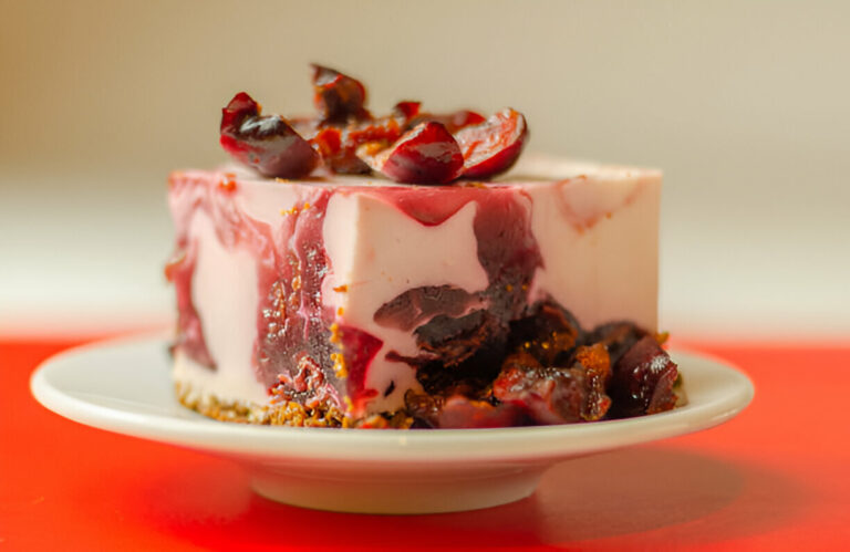 A slice of dessert with a marbled pink and dark purple appearance, topped with dark fruit pieces, on a white plate.