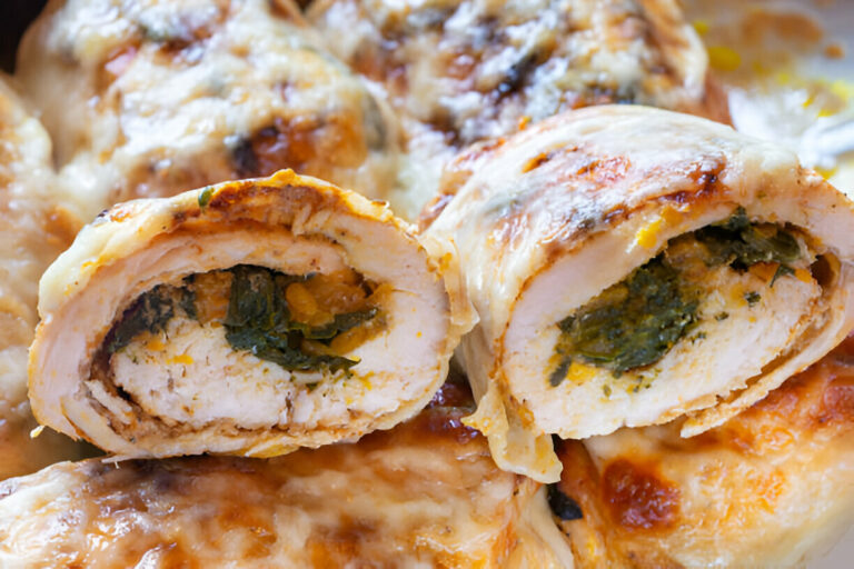 Close-up of a rolled chicken dish filled with spinach and cheese, topped with melted cheese.