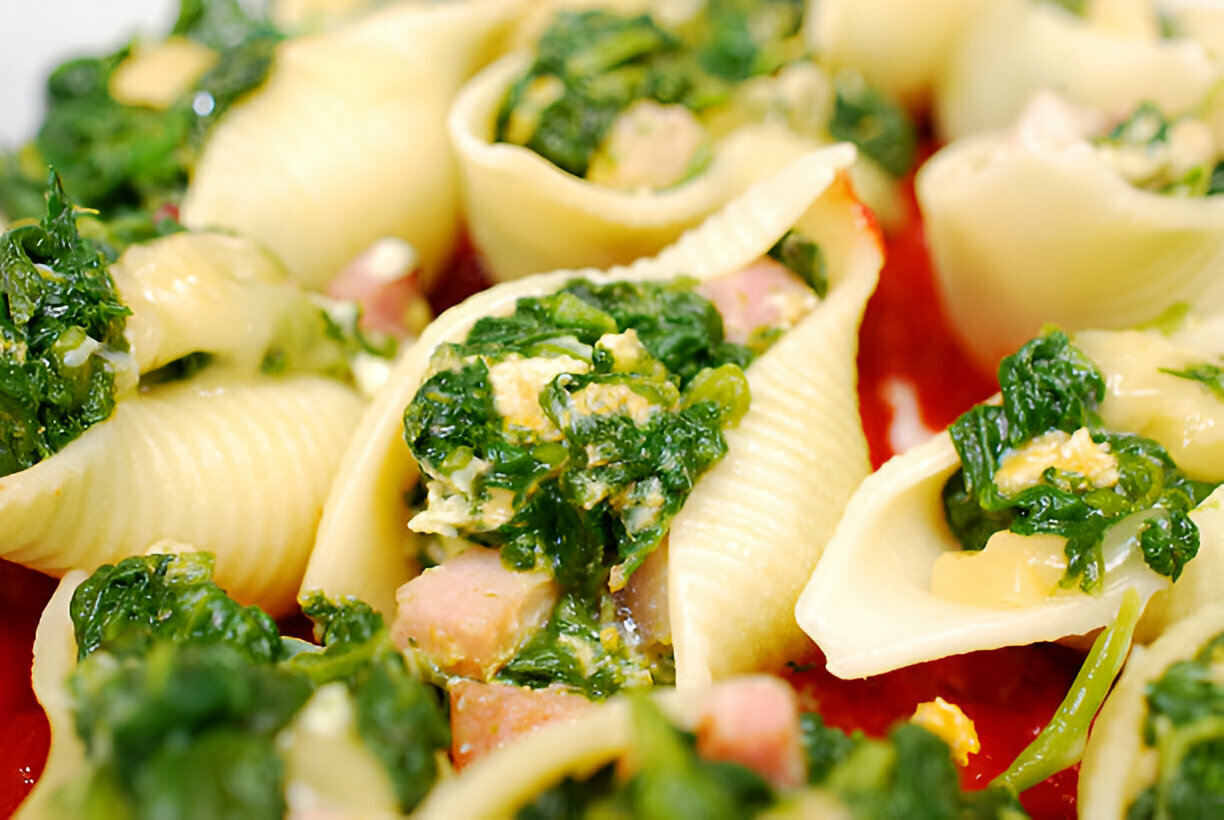 Stuffed pasta shells filled with spinach and cheese on a red sauce background.