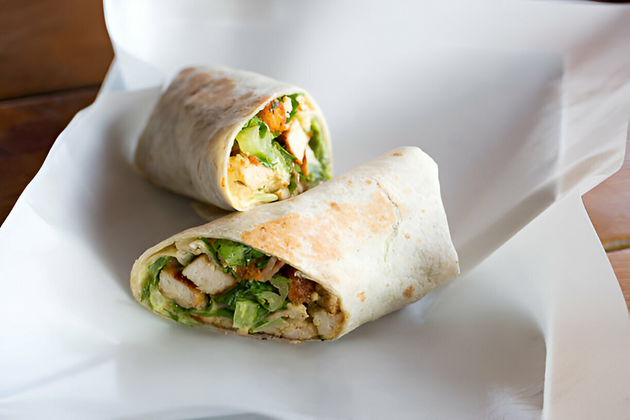 Two rolled wraps filled with chicken and fresh greens on a white surface.