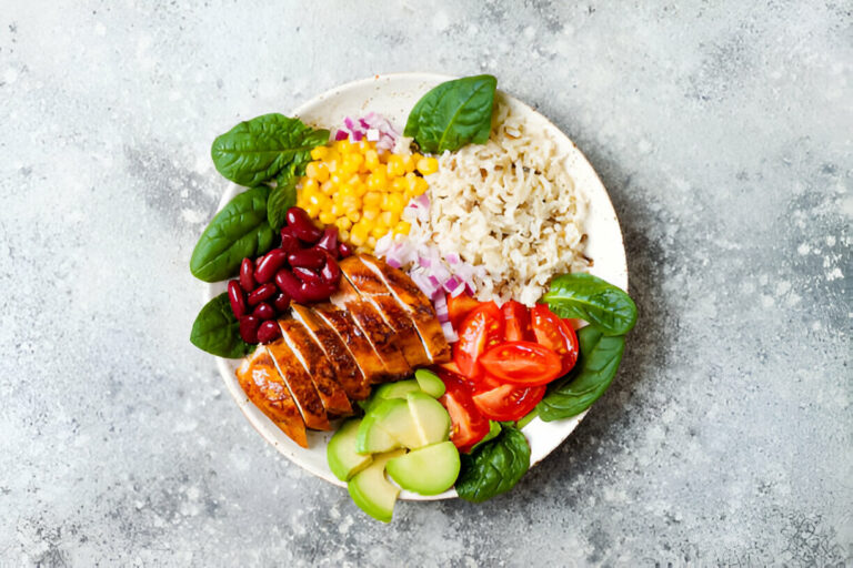 A colorful plate of sliced grilled chicken breast served with rice, mixed vegetables, and fresh greens.