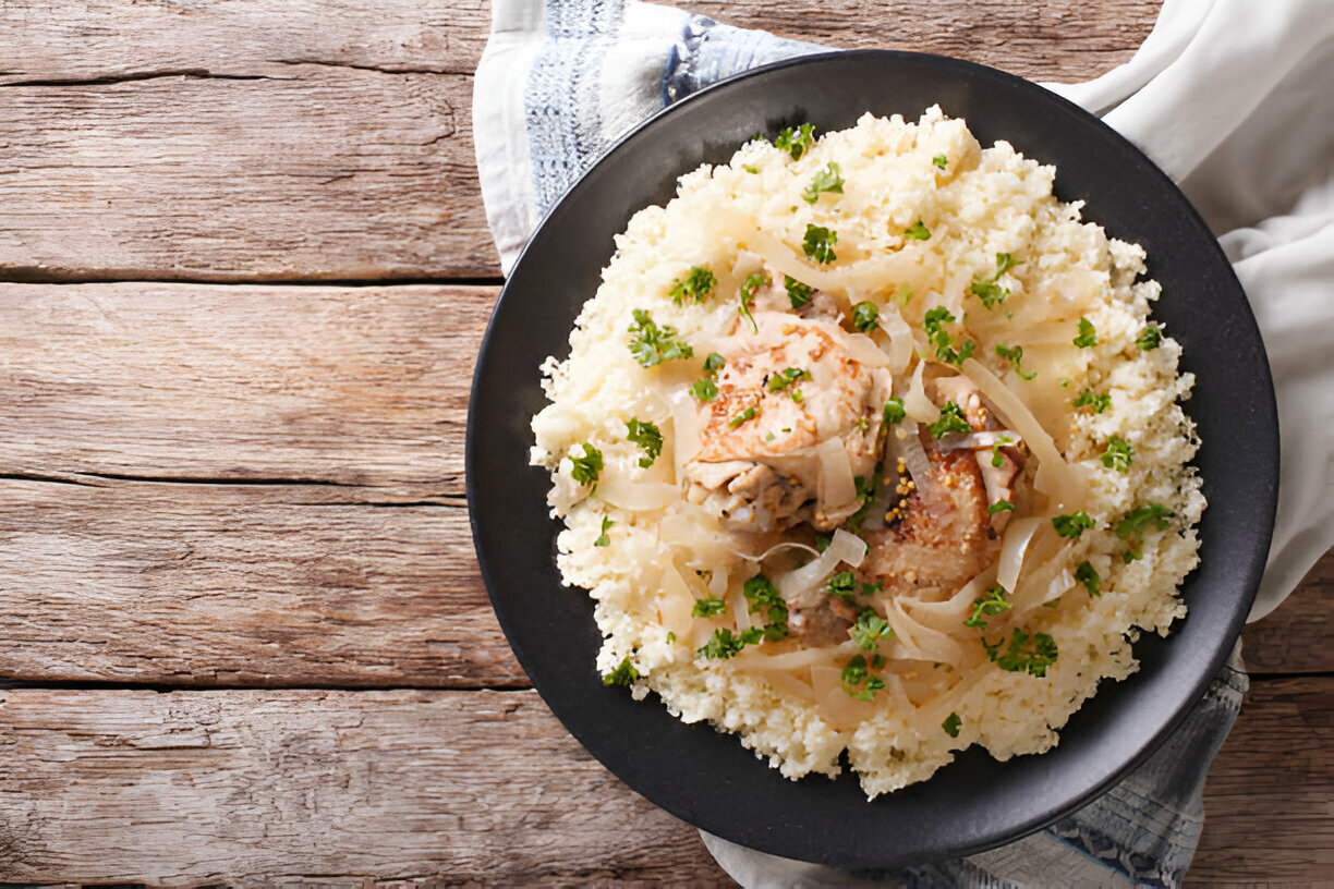 A delicious plate of chicken served over fluffy couscous, garnished with fresh parsley and onions, against a rustic wooden background.