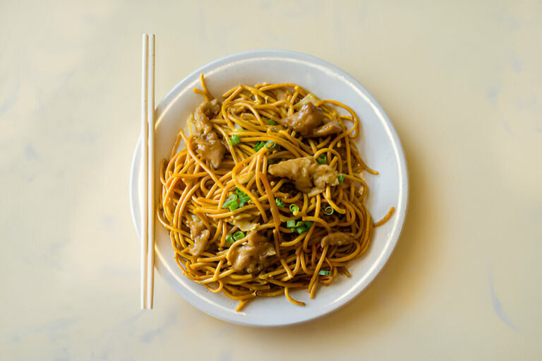 A plate of stir-fried noodles with vegetables and meat, served with chopsticks