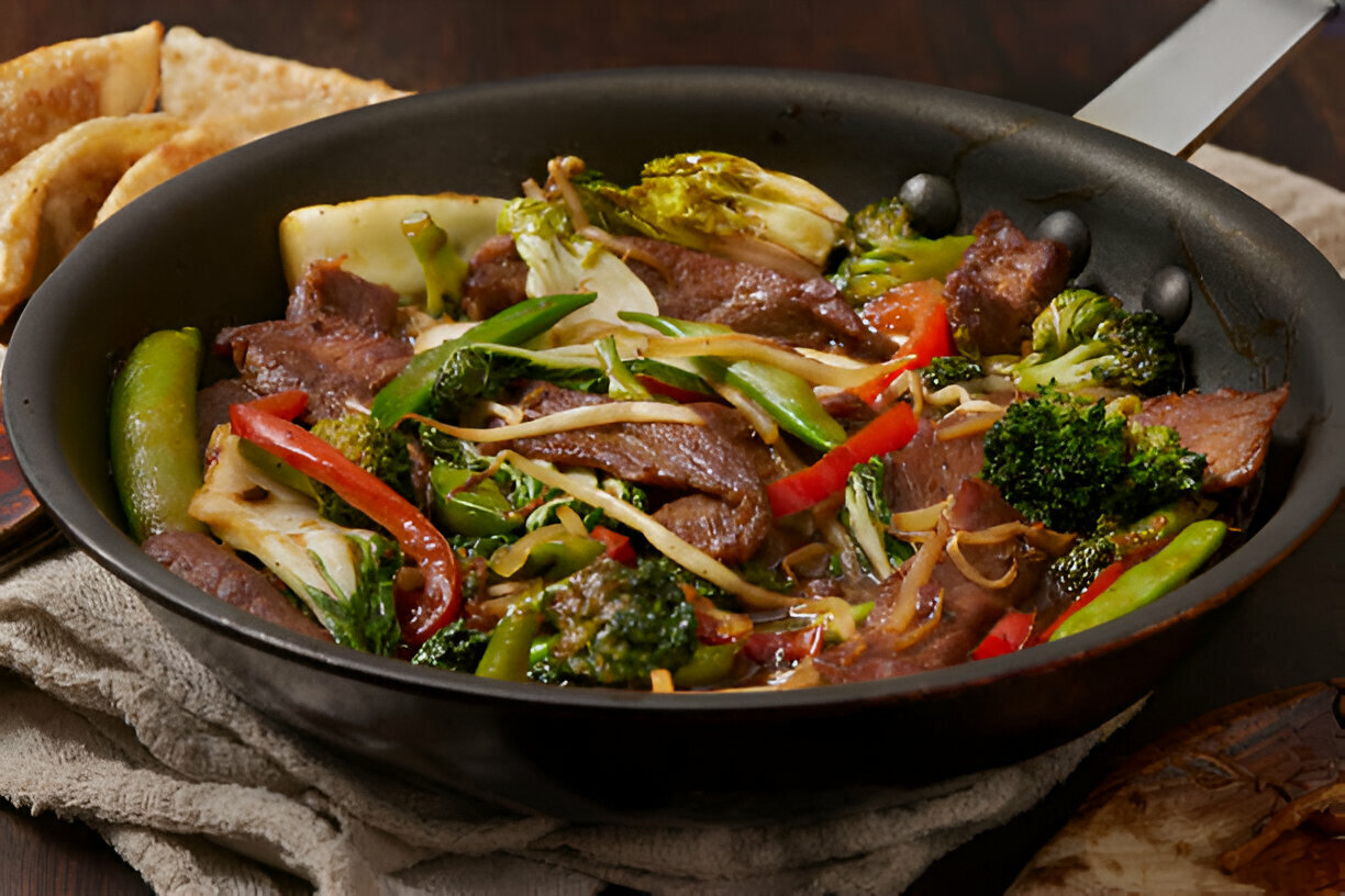 A sizzling stir-fry with beef, colorful vegetables, and a side of crispy dumplings in a black pan.