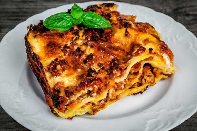 A serving of lasagna topped with fresh basil on a white plate.