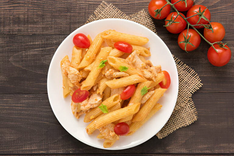 A plate of penne pasta with chicken and cherry tomatoes garnished with fresh herbs on a wooden table.