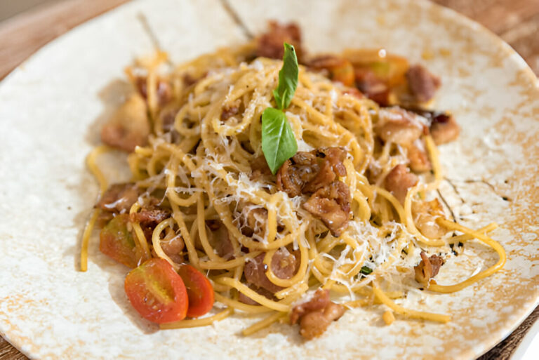 Plate of spaghetti topped with basil, chopped meat, and cherry tomatoes on a rustic wooden table.