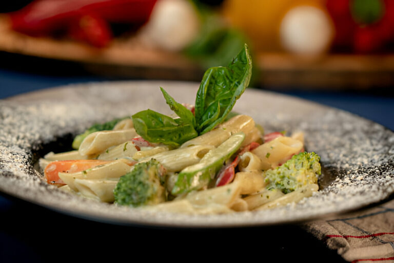 A plate of creamy pasta with broccoli, red peppers, and fresh basil garnish