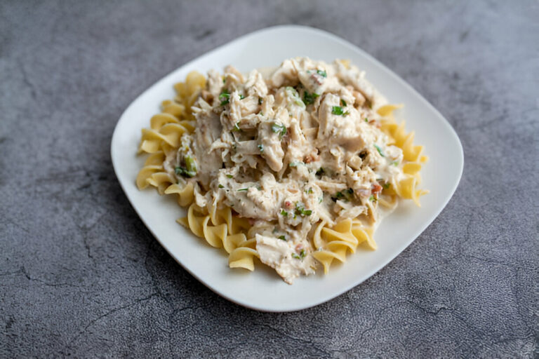 Plate of creamy chicken pasta garnished with herbs on a gray surface.