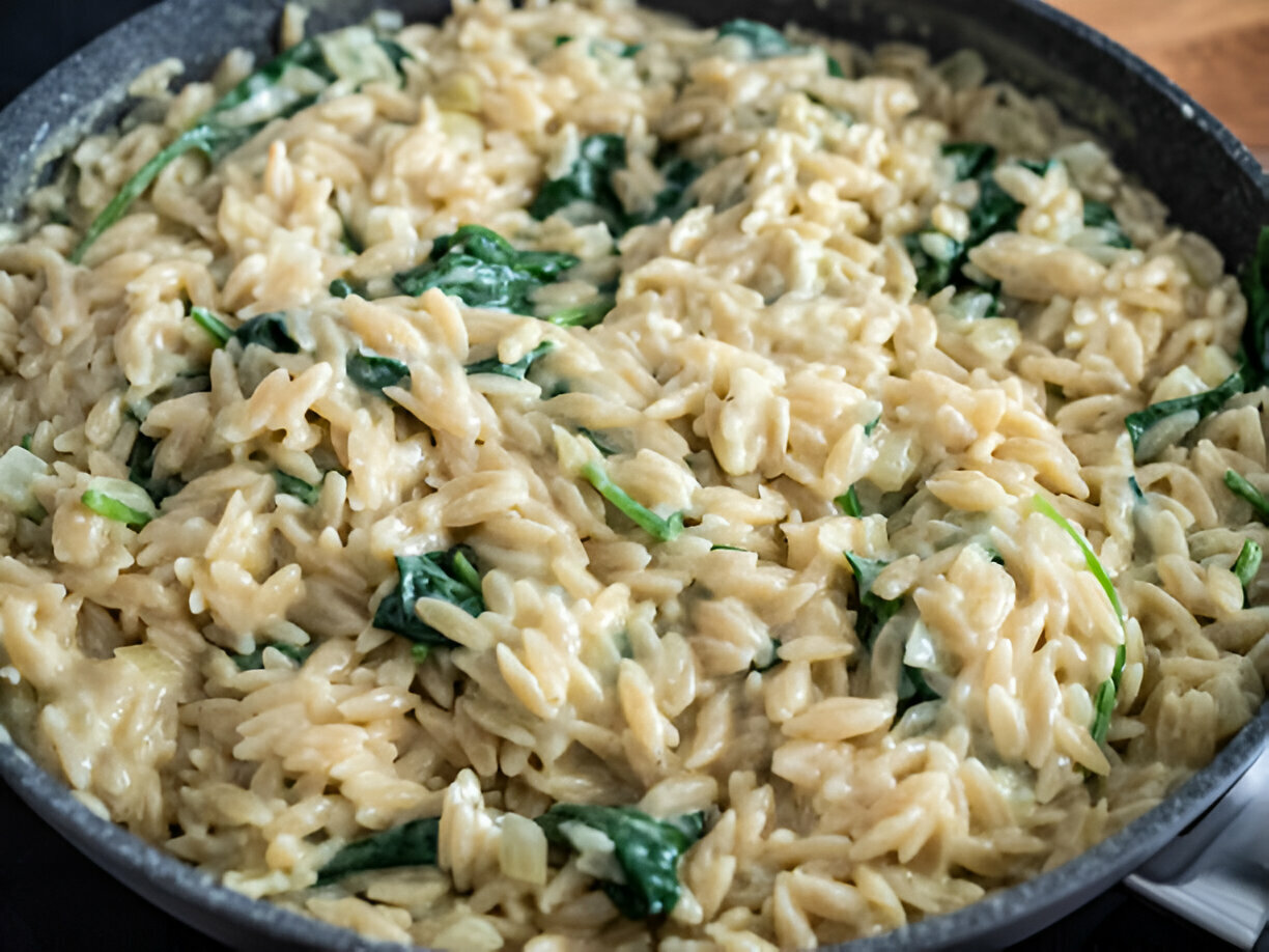 Creamy orzo pasta with spinach cooked in a skillet