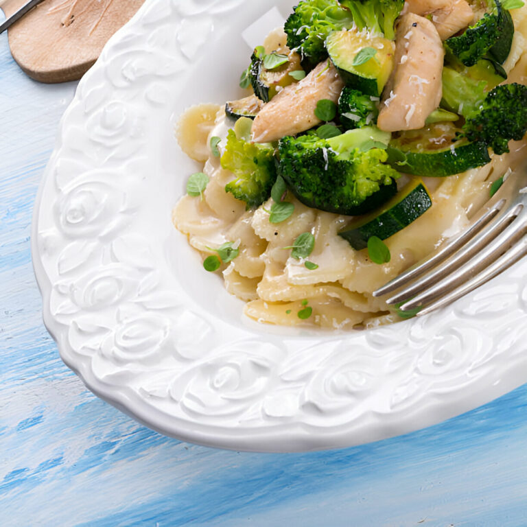 A plate of creamy pasta with broccoli and chicken topped with herbs on a textured blue background.