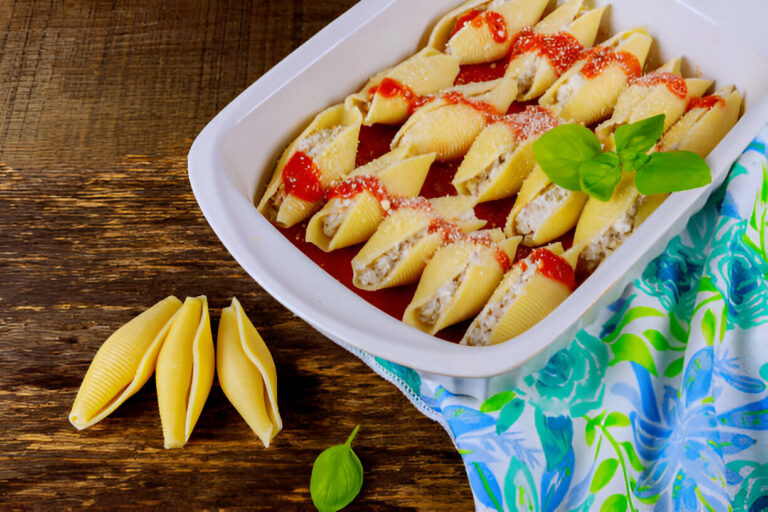 A dish of stuffed pasta shells in marinara sauce, garnished with fresh basil.