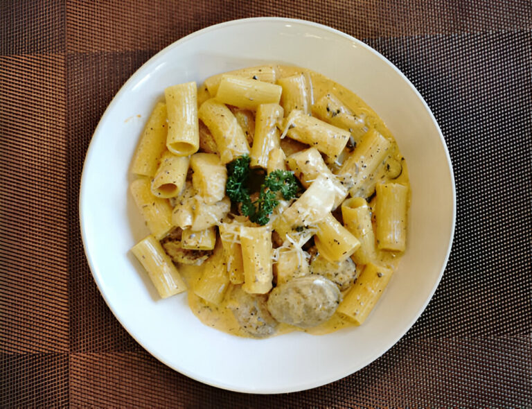 A plate of creamy rigatoni pasta garnished with parsley on a textured brown tablecloth.