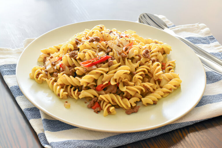 A plate of spiral pasta mixed with ground beef and red peppers on a striped cloth.