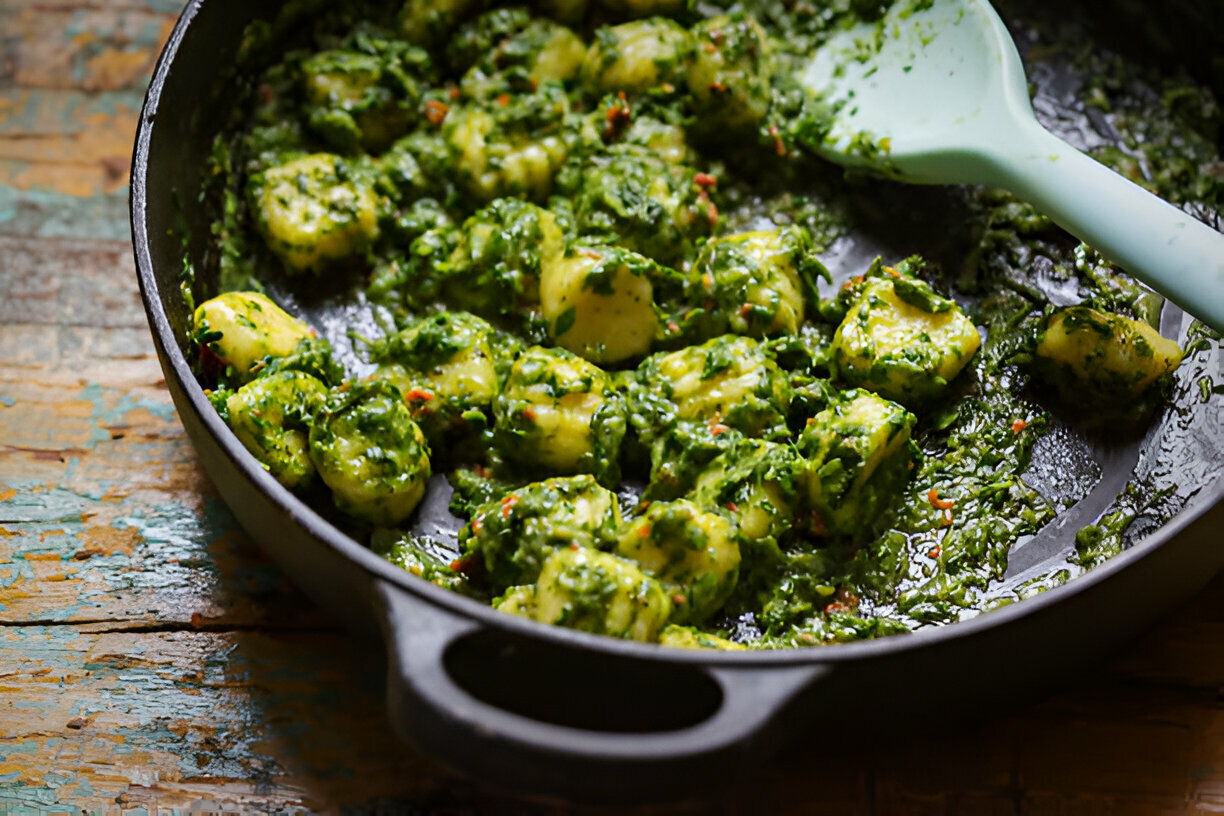 A close-up view of gnocchi coated in a vibrant green sauce in a black skillet.