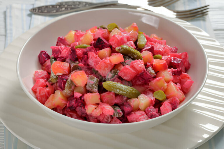 A colorful bowl of salad featuring diced beets, potatoes, pickles, and creamy dressing.