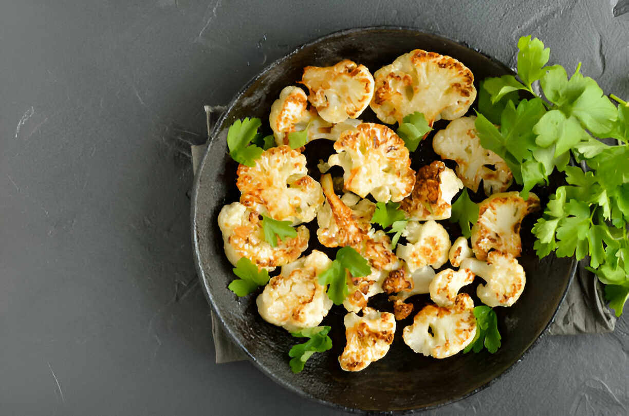 Roasted cauliflower florets garnished with fresh herbs in a cast iron skillet.