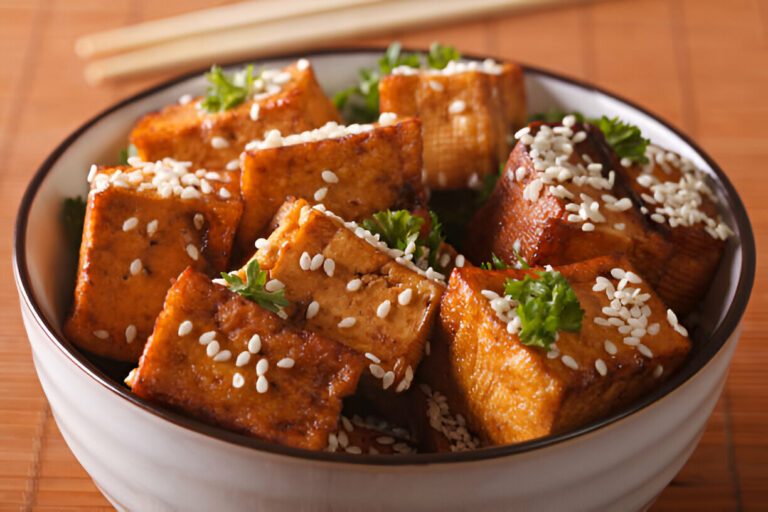 A bowl of golden-brown tofu cubes, garnished with sesame seeds and fresh herbs.