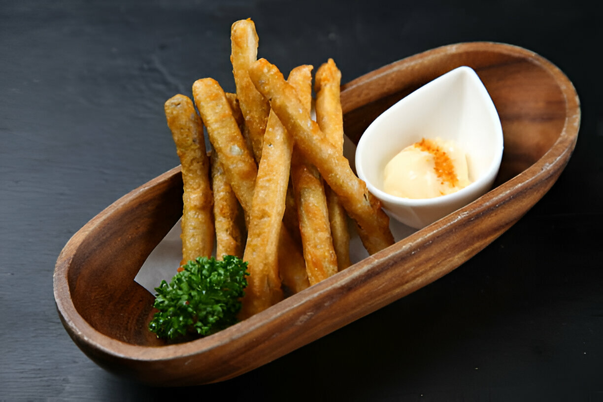 A wooden bowl containing crispy fried sticks and a small dish of creamy sauce, garnished with parsley.