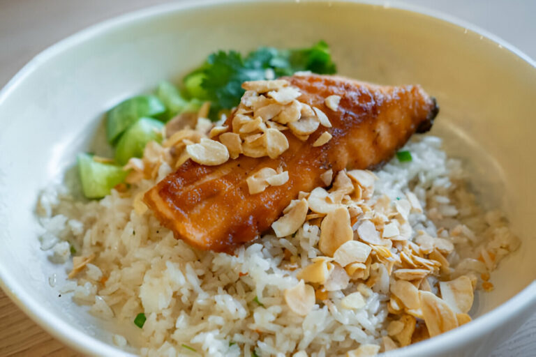 A delicious bowl of rice topped with grilled spicy salmon, sliced almonds, and fresh cilantro.