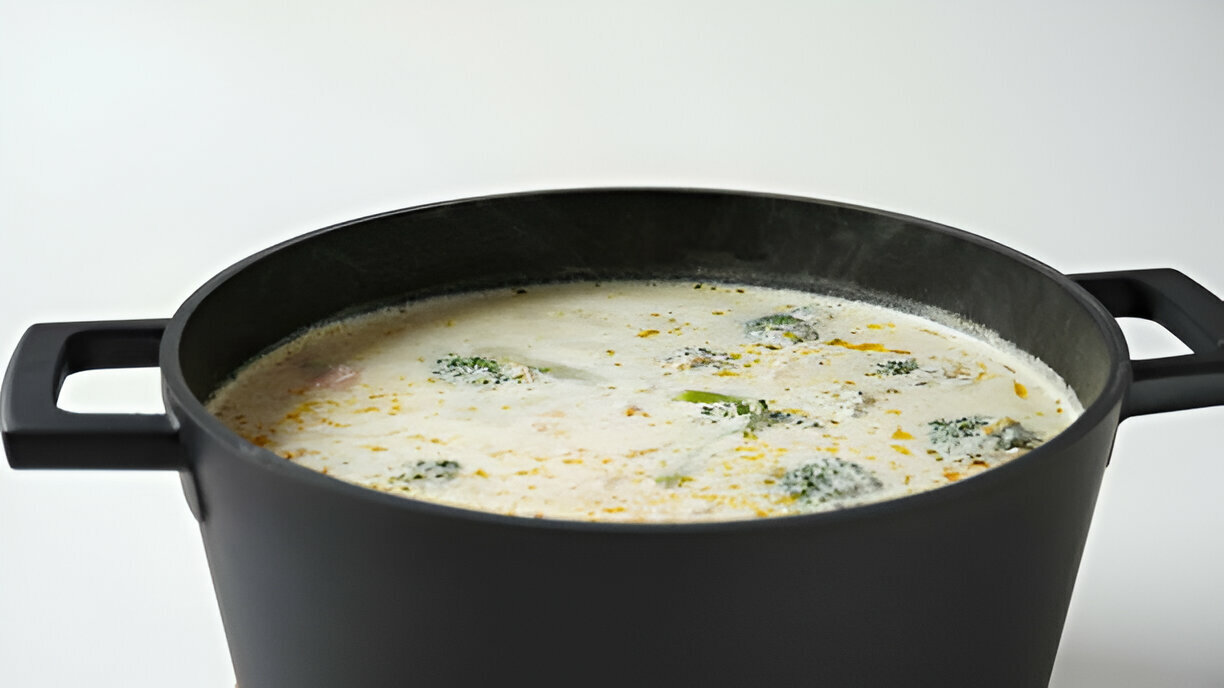 A large black pot filled with creamy soup containing broccoli, viewed from the top