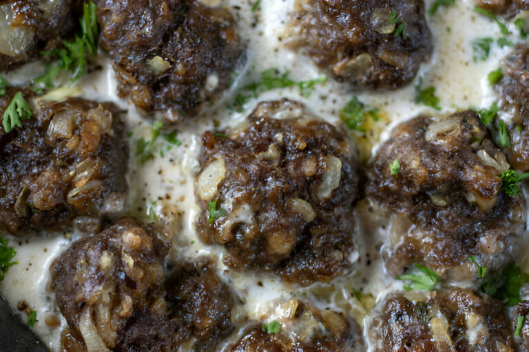 A close-up view of meatballs in creamy sauce, garnished with herbs.