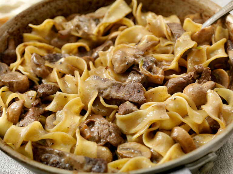 A close-up of cooked egg noodles mixed with beef and mushrooms in a creamy sauce.