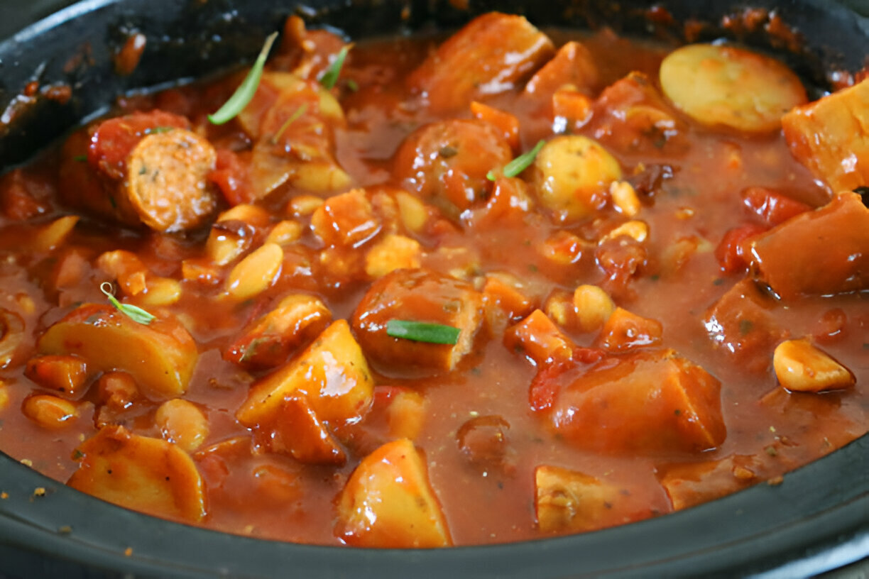 A close-up image of a hearty dish featuring pieces of sausage and potatoes in a rich tomato sauce.