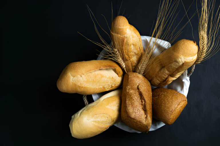 A variety of loaves of bread in a white basket with wheat stalks on a black background.