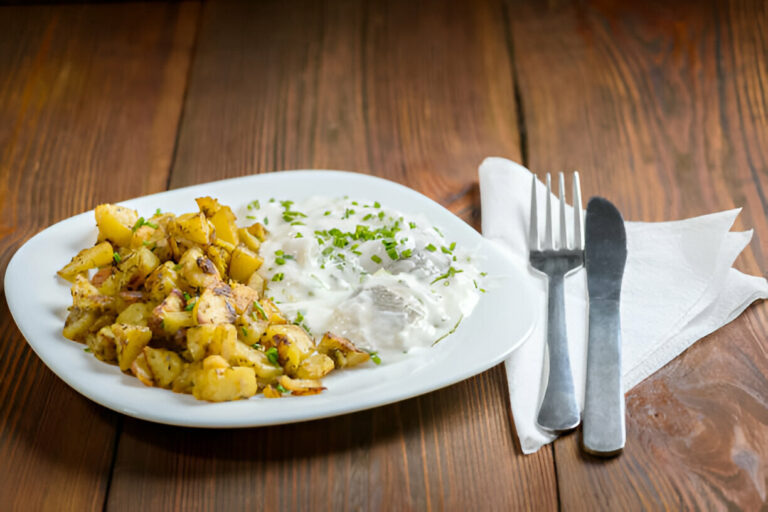 A plate of roasted potatoes served with yogurt and herbs on a wooden table.