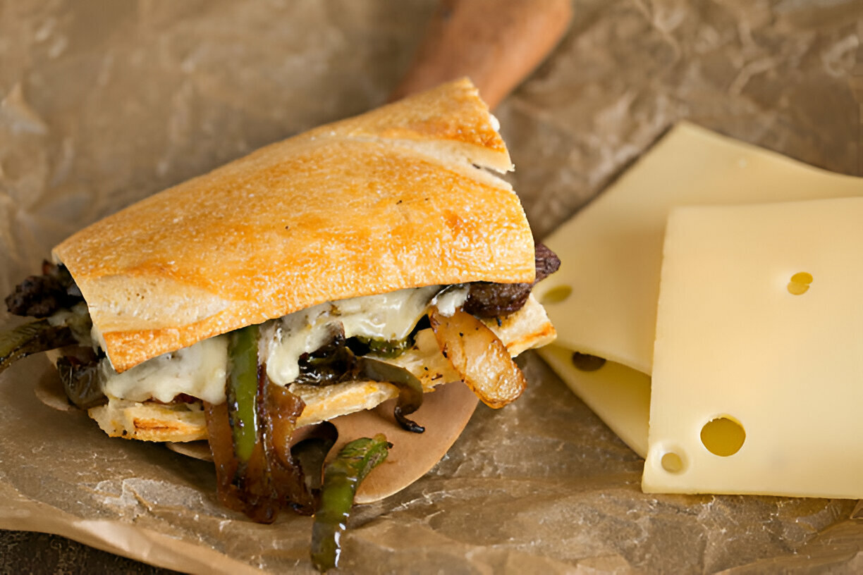 Delicious sandwich filled with grilled beef, peppers, and melted cheese on a wooden board.