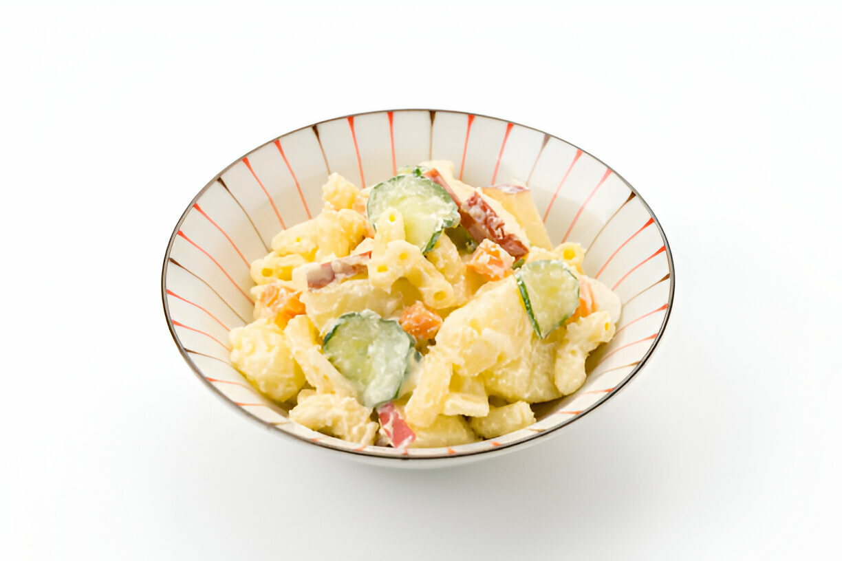 A bowl of creamy pasta salad with cucumbers, carrots, and bits of meat, presented in a stylish dish.