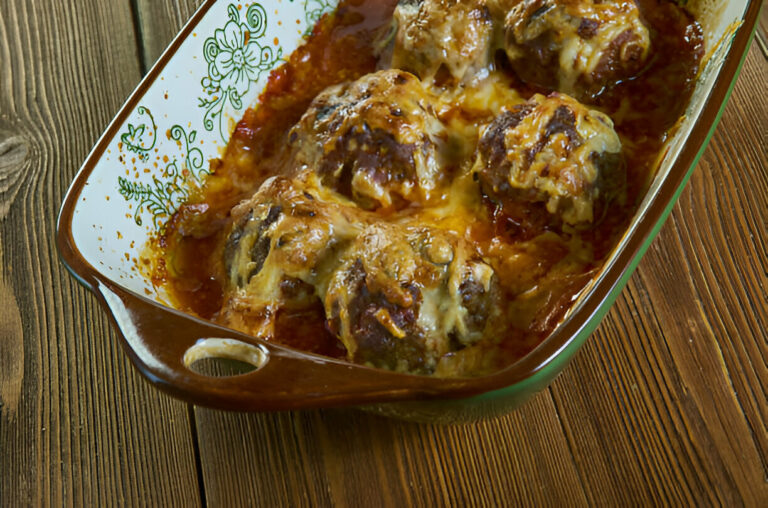 A dish of baked meatballs covered in melted cheese and marinara sauce, served in an oval ceramic baking dish with floral design.