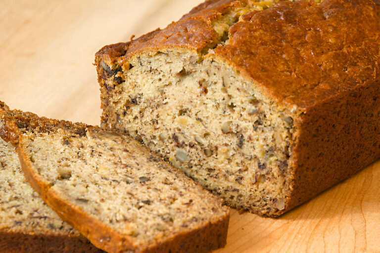 Freshly baked banana bread loaf with slices cut, placed on a wooden surface.