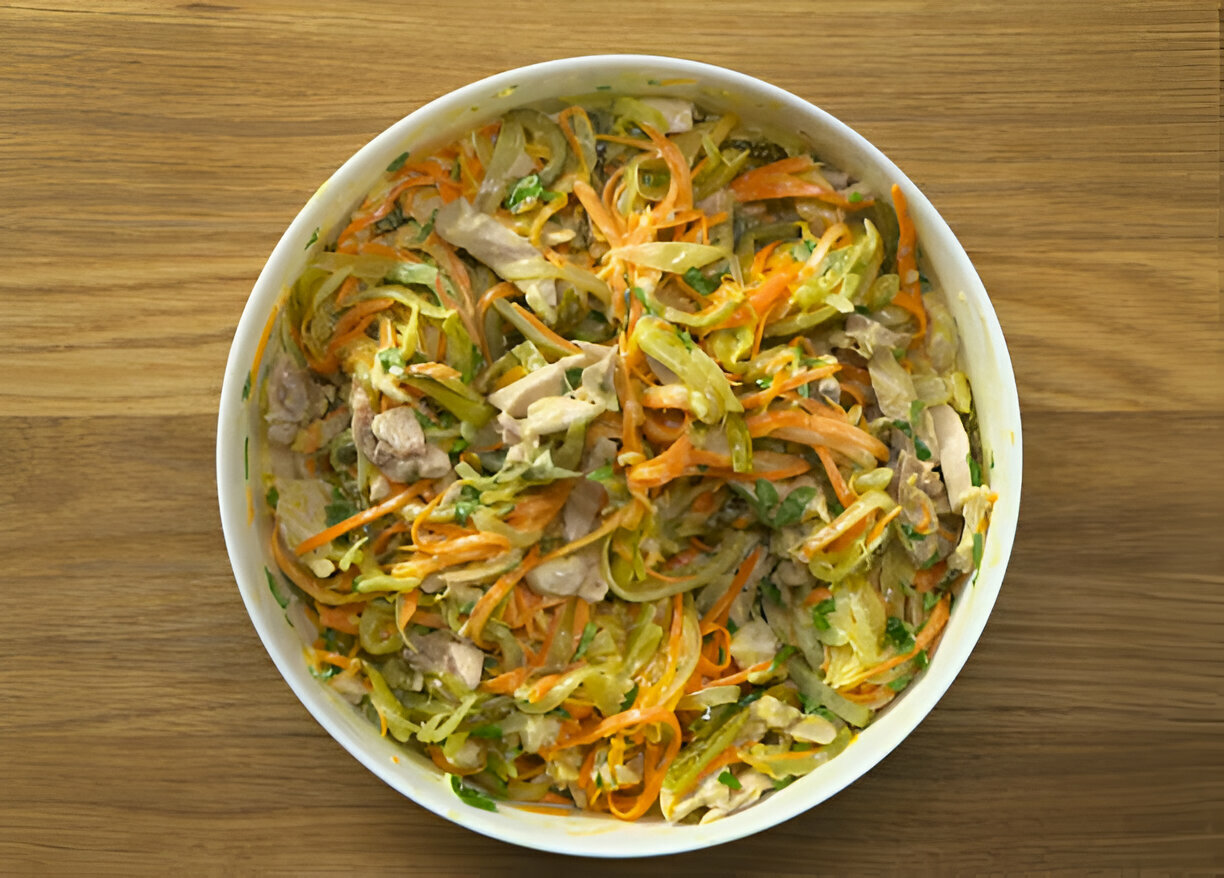 A colorful bowl of mixed salad with shredded carrots, cabbage, and pieces of chicken on a wooden surface.