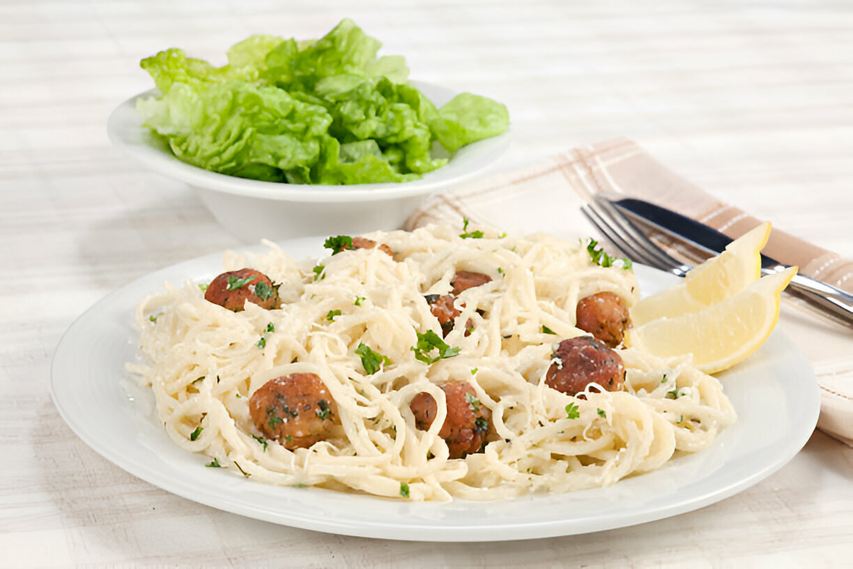 A plate of spaghetti with meatballs, garnished with parsley and served with lemon wedges, alongside a bowl of fresh lettuce.